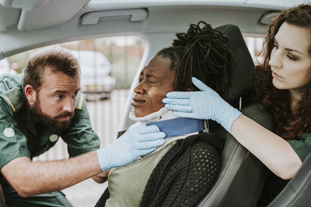 Emergency responders assisting a crying patient with a neck injury inside a vehicle, highlighting the urgency of medical care for injury cases.